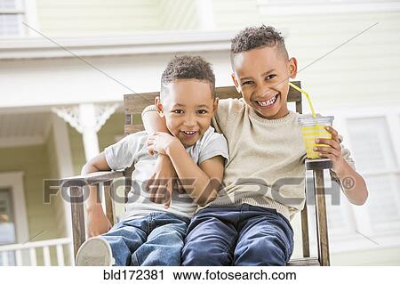 Stock Image - Brothers hugging in armchair in backyard. Fotosearch