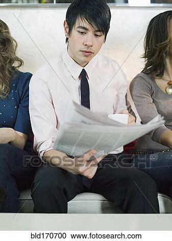 Stock Image - Businessman reading newspaper on sofa. Fotosearch