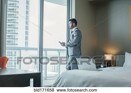 Stock Photo - Businessman using cell phone at hotel window. Fotosearch
