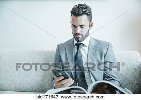 Stock Photo - Businessman using cell phone on sofa. Fotosearch