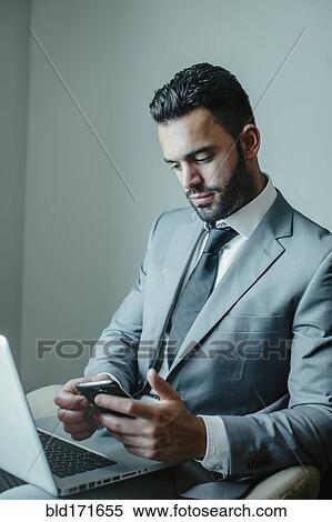 Stock Photography - Businessman using laptop and cell phone in armchair. Fotosearch
