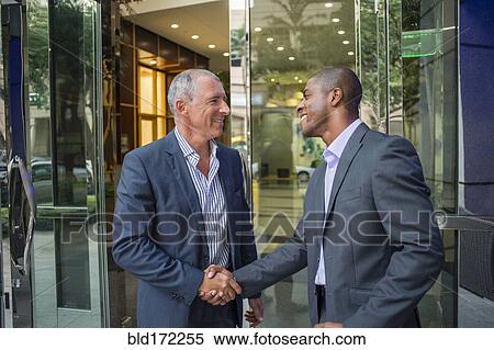 Stock Photography - Businessmen shaking hands at office building. Fotosearch