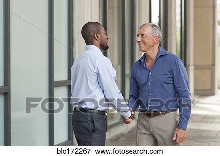 Stock Photo - Businessmen shaking hands in city. Fotosearch