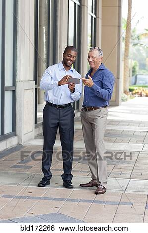 Stock Photograph - Businessmen using cell phone on city sidewalk. Fotosearch