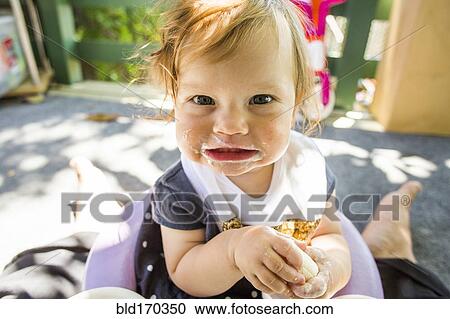 Stock Image - Caucasian baby girl eating on patio. Fotosearch