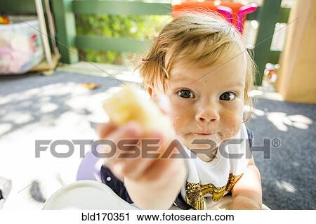 Stock Image - Caucasian baby girl eating on patio. Fotosearch