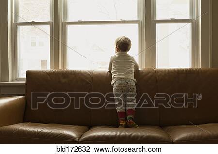 Stock Image - Caucasian boy looking out living room window. Fotosearch