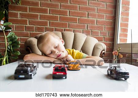 Stock Image - Caucasian boy playing with toy cars at desk. Fotosearch