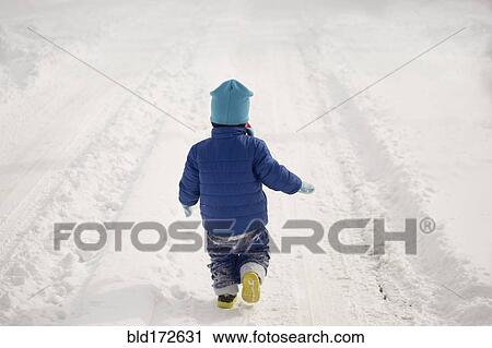 Stock Image - Caucasian boy walking in tire tracks in snow. Fotosearch