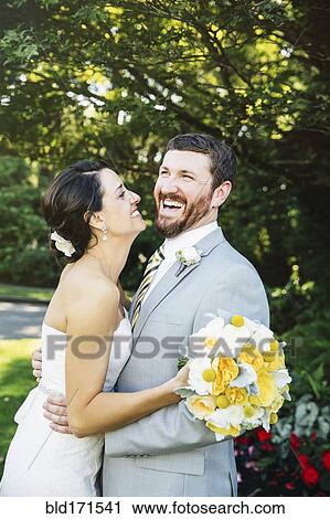 Stock Image - Caucasian bride and groom hugging in garden. Fotosearch
