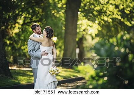 Stock Image - Caucasian bride and groom hugging on rural road. Fotosearch