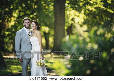 Stock Image - Caucasian bride and groom hugging on rural road. Fotosearch