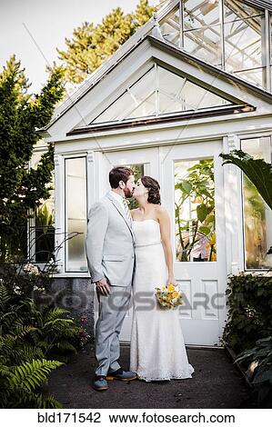 Stock Image - Caucasian bride and groom kissing in garden. Fotosearch