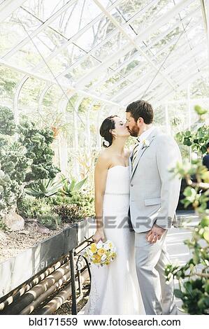 Stock Photo - Caucasian bride and groom kissing in greenhouse. Fotosearch