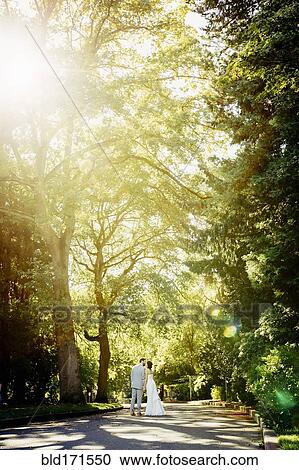 Stock Image - Caucasian bride and groom kissing on rural road. Fotosearch
