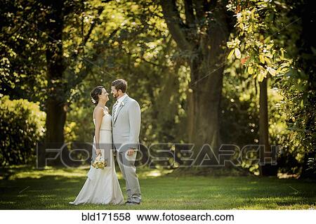 Stock Photo - Caucasian bride and groom walking in grass. Fotosearch