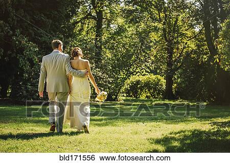 Stock Photograph - Caucasian bride and groom walking in grass. Fotosearch