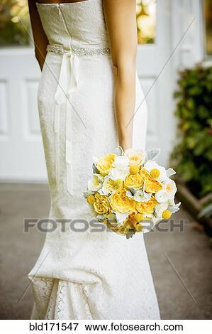 Stock Photo - Caucasian bride holding bouquet in garden. Fotosearch