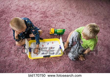 Stock Image - Caucasian brothers playing hockey game on floor. Fotosearch