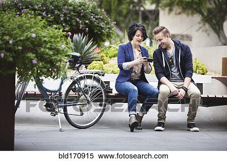Stock Photography - Caucasian business people using cell phone on bench. Fotosearch
