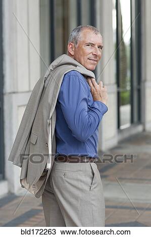 Stock Image - Caucasian businessman carrying jacket on city sidewalk. Fotosearch