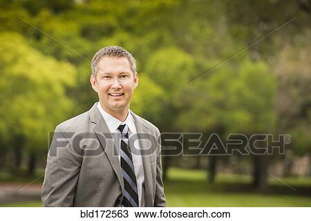 Stock Image - Caucasian businessman smiling in park. Fotosearch