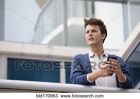 Stock Image - Caucasian businessman using cell phone on balcony. Fotosearch