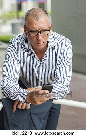 Stock Photo - Caucasian businessman using cell phone at banister. Fotosearch
