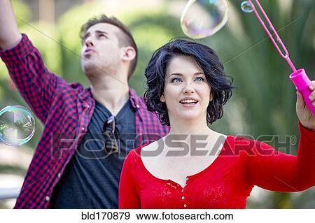 Stock Photo - Caucasian couple blowing bubbles outdoors. Fotosearch