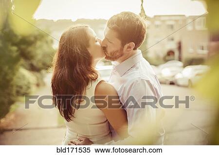 Stock Photography - Caucasian couple kissing on sidewalk. Fotosearch