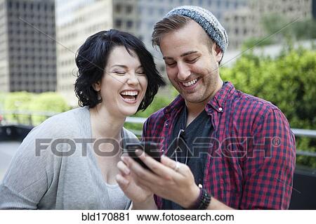 Stock Image - Caucasian couple using cell phone in city. Fotosearch