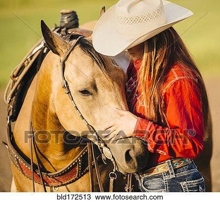 Stock Image - Caucasian cowgirl petting horse on ranch. Fotosearch