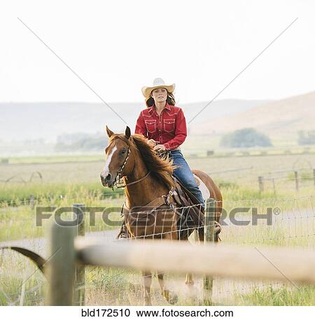 Stock Image - Caucasian cowgirl riding horse on ranch. Fotosearch