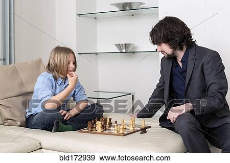Stock Photo - Caucasian father and son playing chess on sofa. Fotosearch