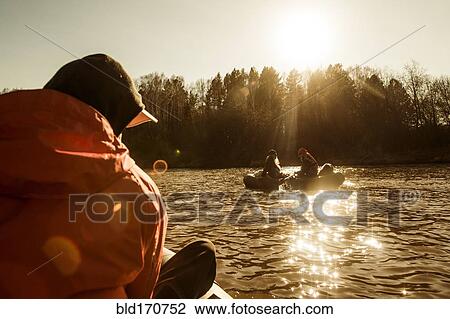 Stock Image - Caucasian fisherman sitting in canoe on river. Fotosearch