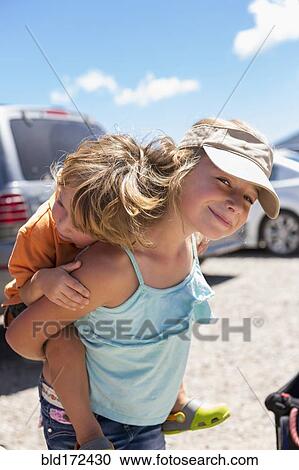 Stock Image - Caucasian girl carrying brother piggyback. Fotosearch