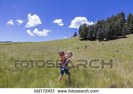 Stock Image - Caucasian girl carrying brother piggyback in field. Fotosearch