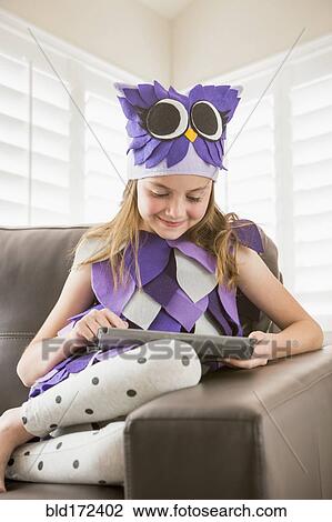 Stock Image - Caucasian girl in costume using digital tablet on sofa. Fotosearch