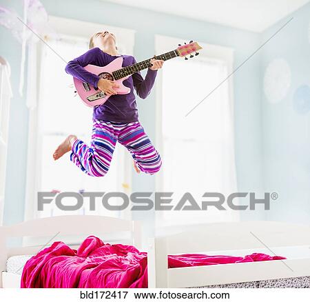 Stock Photo - Caucasian girl playing guitar on bed. Fotosearch