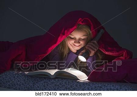 Stock Image - Caucasian girl reading under blanket at night. Fotosearch