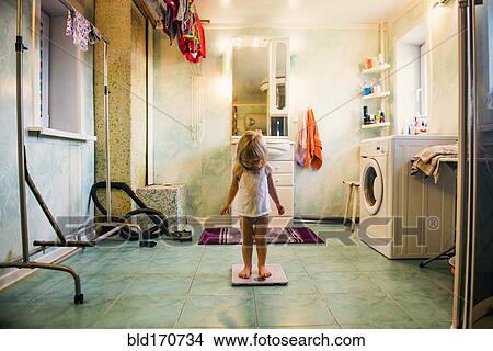 Picture - Caucasian girl standing on scale in bathroom. Fotosearch