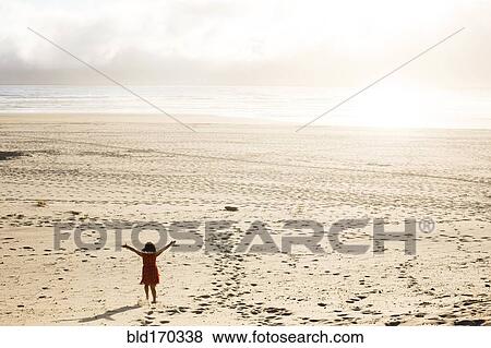 Stock Photo - Caucasian girl standing with arms outstretched on beach. Fotosearch