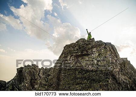 Stock Image - Caucasian hiker cheering on rocky hilltop. Fotosearch