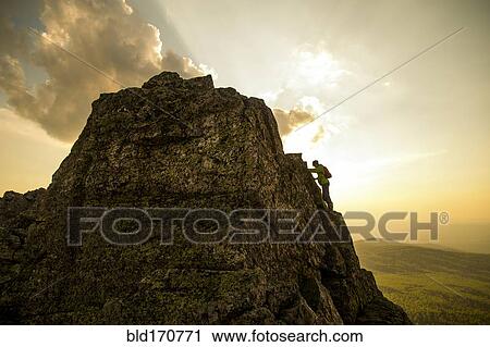 Stock Image - Caucasian hiker climbing on rock formation. Fotosearch