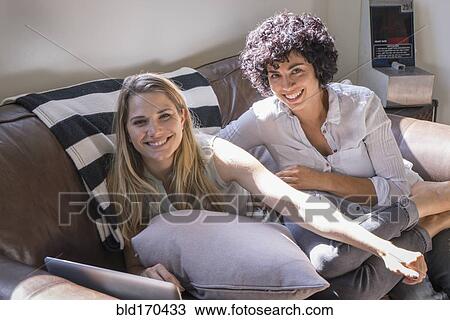 Stock Image - Caucasian lesbian couple smiling on sofa. Fotosearch