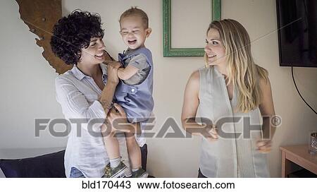 Stock Image - Caucasian lesbian mothers and baby son in living room. Fotosearch