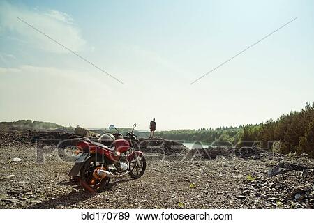 Stock Photo - Caucasian man and motorcycle in rural field. Fotosearch