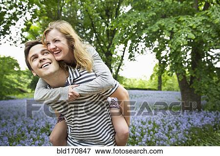 Stock Photo - Caucasian man carrying girlfriend piggyback in field of flowers. Fotosearch