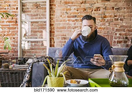 Stock Image - Caucasian man drinking coffee on sofa in living room. Fotosearch
