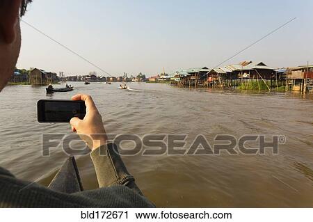 Stock Image - Caucasian man photographing with cell phone on rural river. Fotosearch